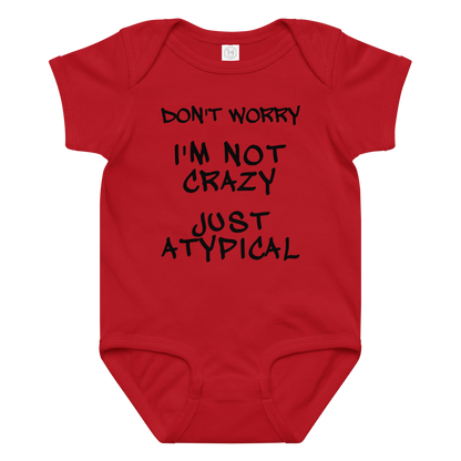 "Don't Worry I'm Not Crazy Just Atypical" printed on a red baby jersey bodysuit laying on a flat surface amongst other clothes