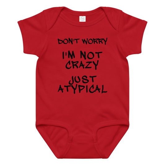 "Don't Worry I'm Not Crazy Just Atypical" printed on a red baby jersey bodysuit laying on a flat surface amongst other clothes