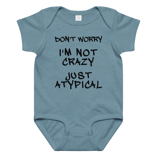 "Don't Worry I'm Not Crazy Just Atypical" printed on a vintage indigo baby jersey bodysuit laying on a flat surface amongst other clothes