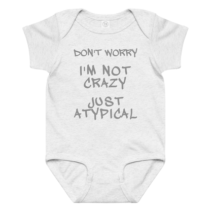 "Don't Worry I'm Not Crazy Just Atypical" printed on a ash baby jersey bodysuit laying on a flat surface amongst other clothes
