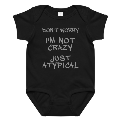 "Don't Worry I'm Not Crazy Just Atypical" printed on a black baby jersey bodysuit laying on a flat surface amongst other clothes