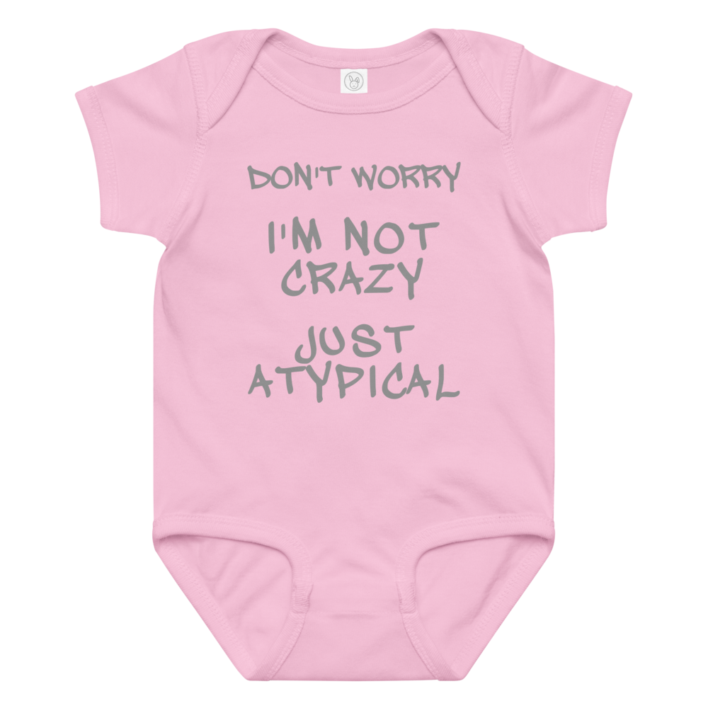 "Don't Worry I'm Not Crazy Just Atypical" printed on a pink baby jersey bodysuit laying on a flat surface amongst other clothes