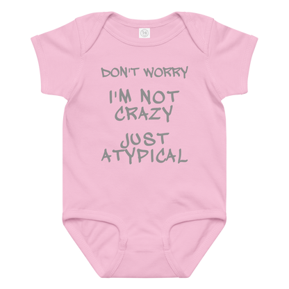 "Don't Worry I'm Not Crazy Just Atypical" printed on a pink baby jersey bodysuit laying on a flat surface amongst other clothes