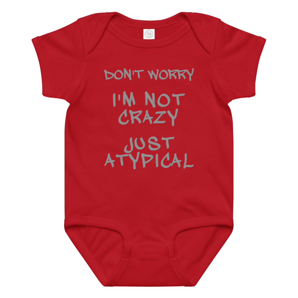 "Don't Worry I'm Not Crazy Just Atypical" printed on a red baby jersey bodysuit laying on a flat surface amongst other clothes