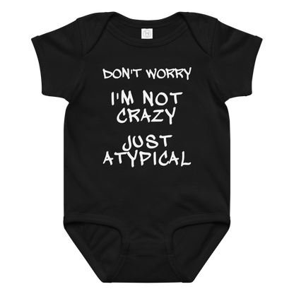 "Don't Worry I'm Not Crazy Just Atypical" printed on a black baby jersey bodysuit laying on a flat surface amongst other clothes