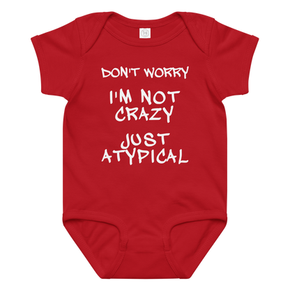 "Don't Worry I'm Not Crazy Just Atypical" printed on a red baby jersey bodysuit laying on a flat surface amongst other clothes