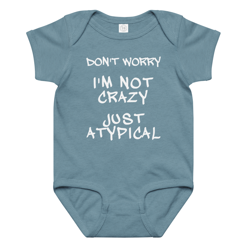 "Don't Worry I'm Not Crazy Just Atypical" printed on a vintage indigo baby jersey bodysuit laying on a flat surface amongst other clothes