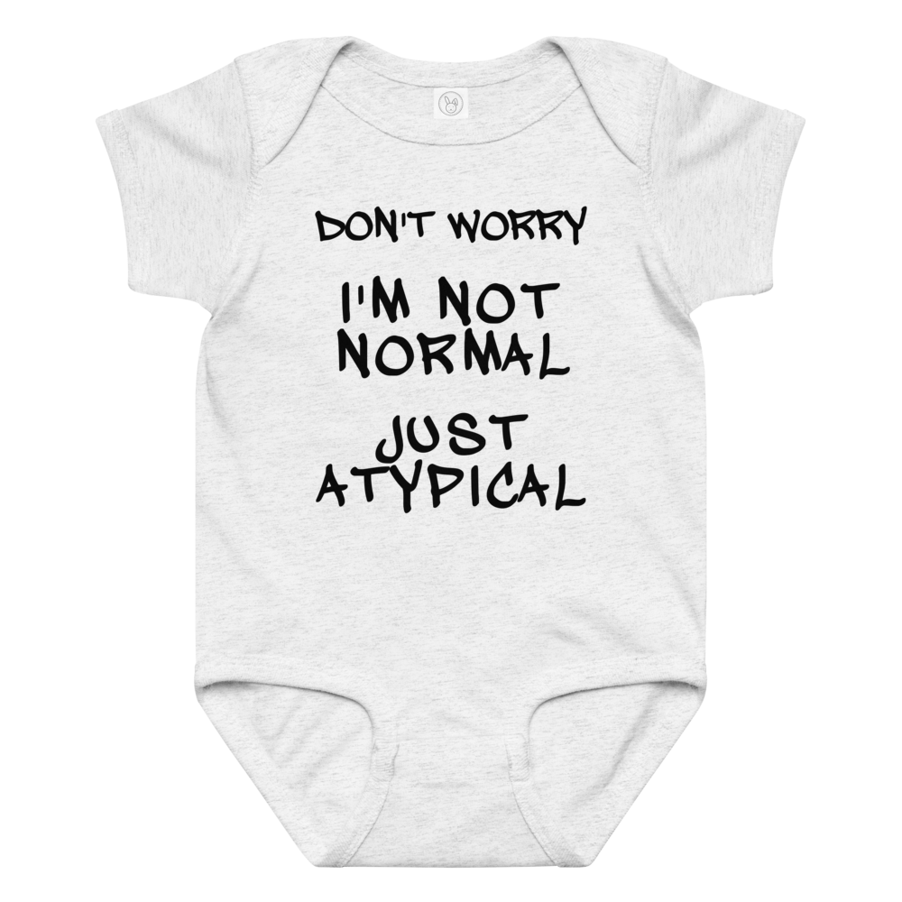 "Don't Worry I'm Not Normal Just Atypical" printed on a ash baby jersey bodysuit laying on a flat surface amongst other clothes