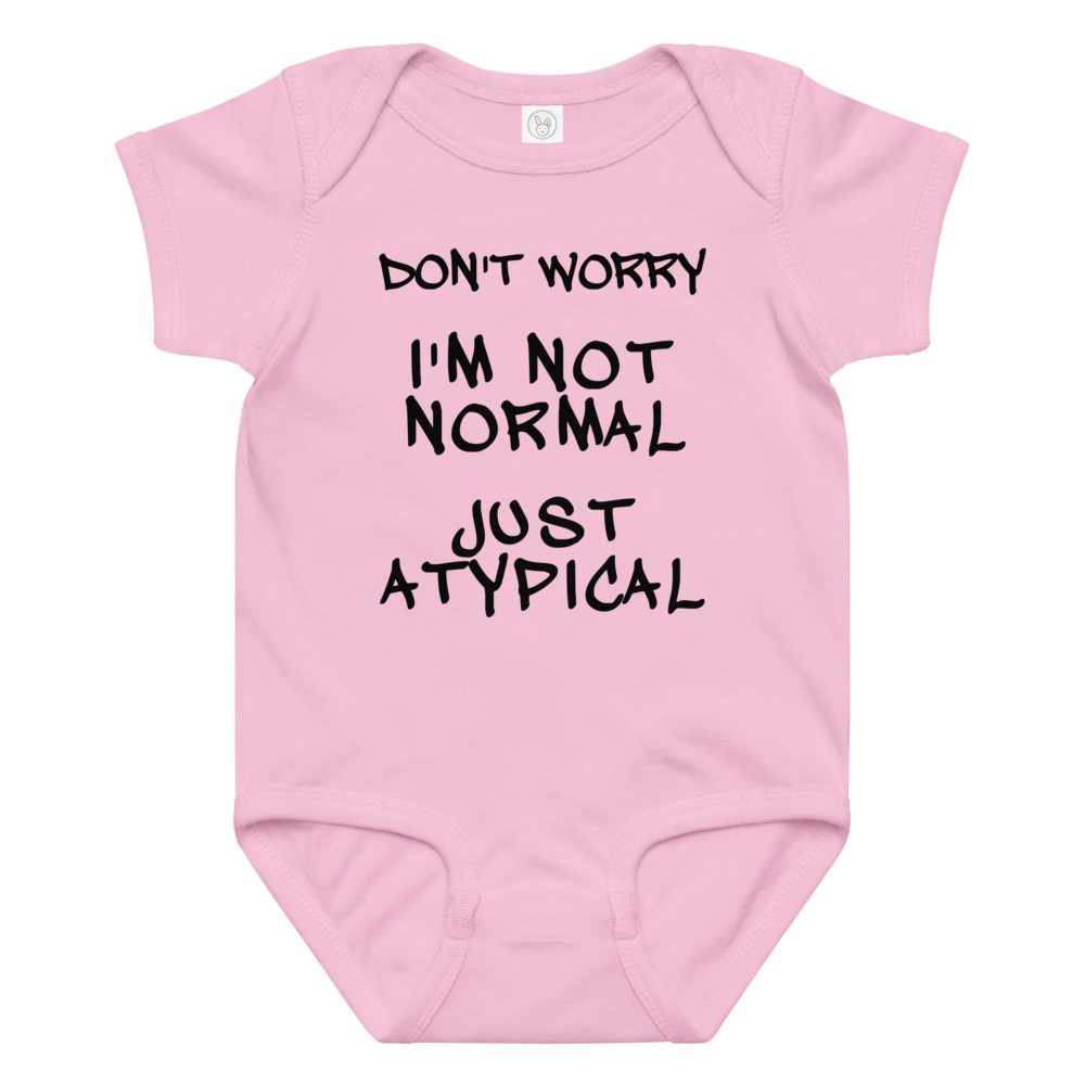 "Don't Worry I'm Not Normal Just Atypical" printed on a pink baby jersey bodysuit laying on a flat surface amongst other clothes