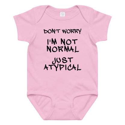 "Don't Worry I'm Not Normal Just Atypical" printed on a pink baby jersey bodysuit laying on a flat surface amongst other clothes