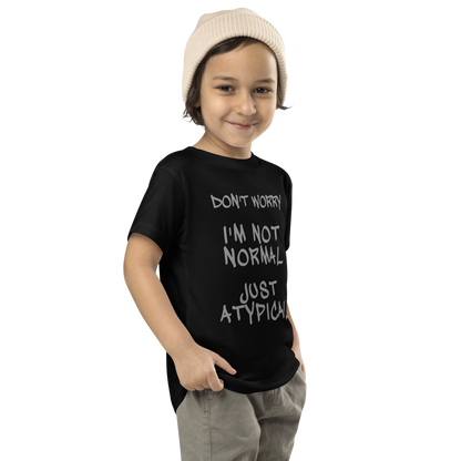 "Don't Worry I'm Not Normal Just Atypical" printed on a black toddler short sleeve tee worn by a male who is also wearing a knit cap