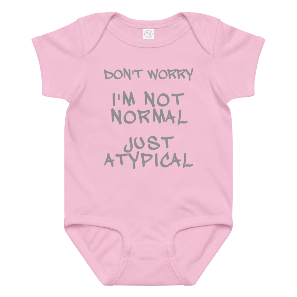 "Don't Worry I'm Not Normal Just Atypical" printed on a pink baby jersey bodysuit laying on a flat surface amongst other clothes
