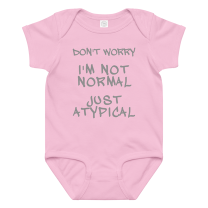 "Don't Worry I'm Not Normal Just Atypical" printed on a pink baby jersey bodysuit laying on a flat surface amongst other clothes