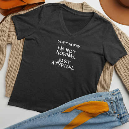 "Don't Worry I'm Not Normal Just Atypical" printed on a dark grey heather women's relaxed v-neck t-shirt laying on a flat surface amongst other clothes