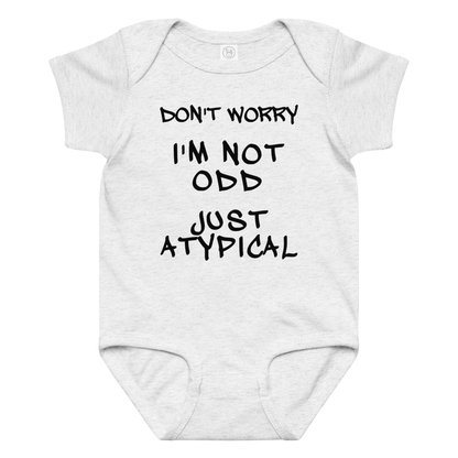 "Don't Worry I'm Not Odd Just Atypical" printed on a ash baby jersey bodysuit laying on a flat surface amongst other clothes