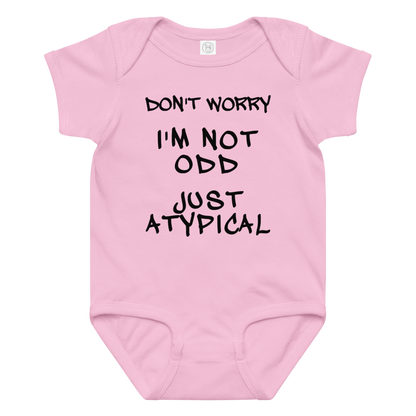 "Don't Worry I'm Not Odd Just Atypical" printed on a pink baby jersey bodysuit laying on a flat surface amongst other clothes