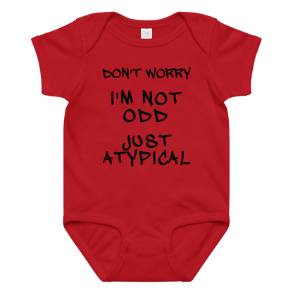 "Don't Worry I'm Not Odd Just Atypical" printed on a red baby jersey bodysuit laying on a flat surface amongst other clothes