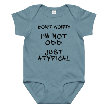 "Don't Worry I'm Not Odd Just Atypical" printed on a vintage indigo baby jersey bodysuit laying on a flat surface amongst other clothes