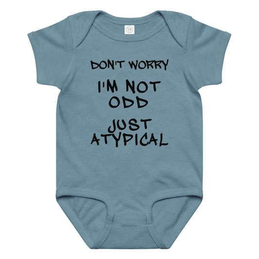 "Don't Worry I'm Not Odd Just Atypical" printed on a vintage indigo baby jersey bodysuit laying on a flat surface amongst other clothes