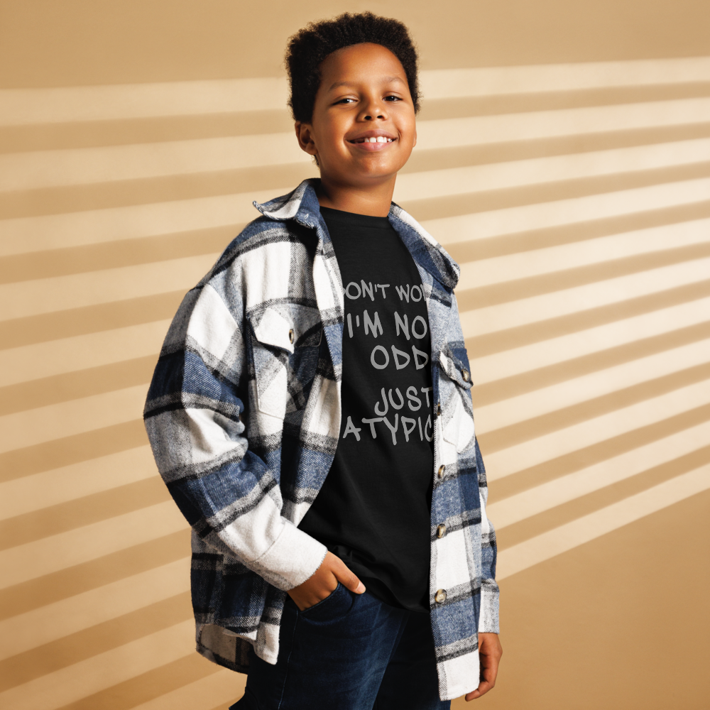 "Don't Worry I'm Not Odd Just Atypical" printed on a black youth classic tee worn by a male also wearing a jacket