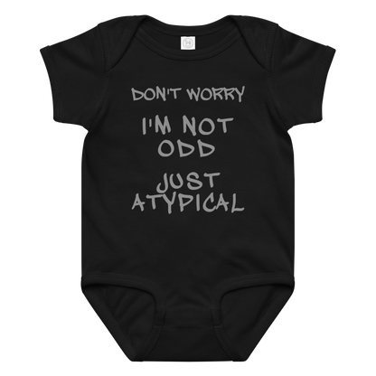 "Don't Worry I'm Not Odd Just Atypical" printed on a black baby jersey bodysuit laying on a flat surface amongst other clothes