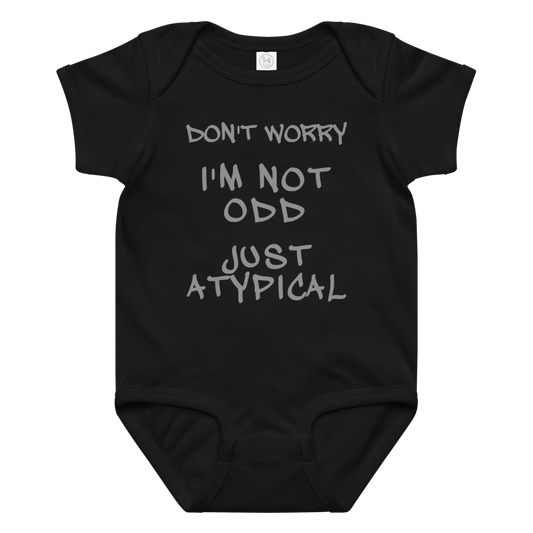 "Don't Worry I'm Not Odd Just Atypical" printed on a black baby jersey bodysuit laying on a flat surface amongst other clothes