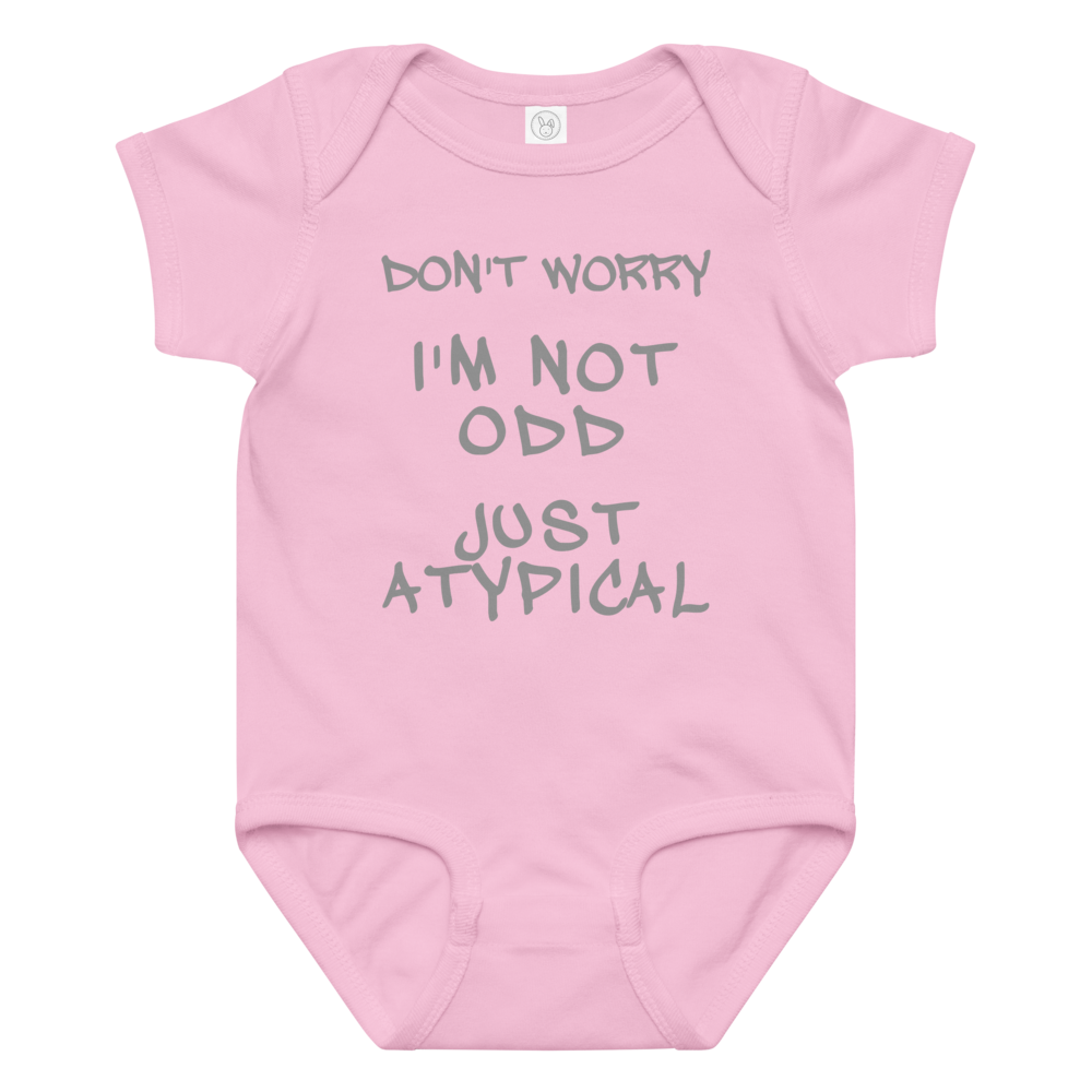 "Don't Worry I'm Not Odd Just Atypical" printed on a pink baby jersey bodysuit laying on a flat surface amongst other clothes