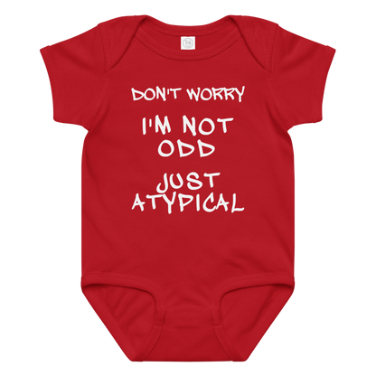 "Don't Worry I'm Not Odd Just Atypical" printed on a red baby jersey bodysuit laying on a flat surface amongst other clothes