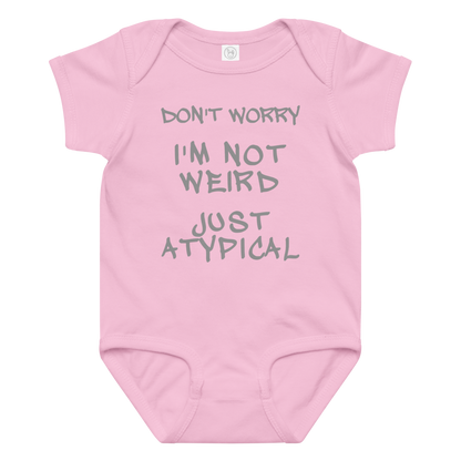 "Don't Worry I'm Not Weird Just Atypical" printed on a pink baby jersey bodysuit laying on a flat surface amongst other clothes