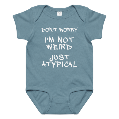 "Don't Worry I'm Not Weird Just Atypical" printed on a vintage indigo baby jersey bodysuit laying on a flat surface amongst other clothes