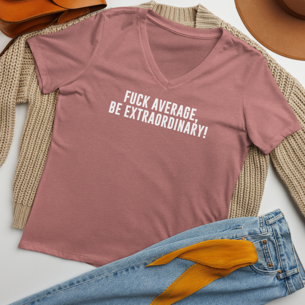 "Fuck Average, Be Extraordinary!" printed on a heather mauve women's relaxed v-neck t-shirt laying on a flat surface amongst other clothes