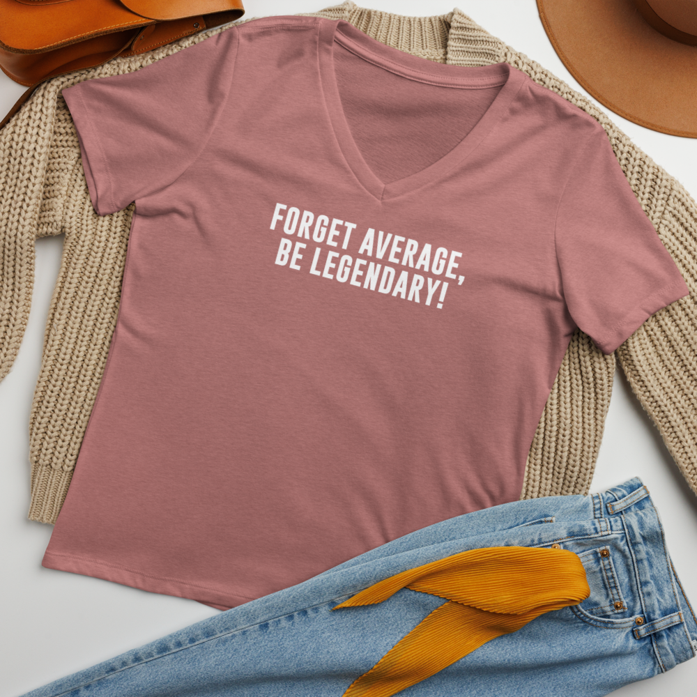 "Forget Average, Be Legendary!" printed on a heather mauve women's relaxed v-neck t-shirt laying on a flat surface amongst other clothes