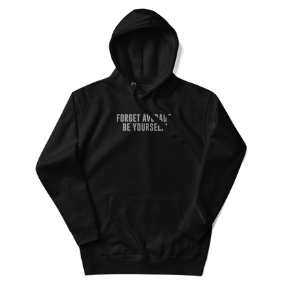 "Forget Average, Be Yourself!" printed on a black unisex hoodie laying on a flat surface with the hood up