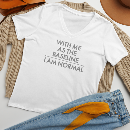 "With me as the baseline, I am normal" printed on a solid white blend women's relaxed v-neck t-shirt laying on a flat surface amongst other clothes