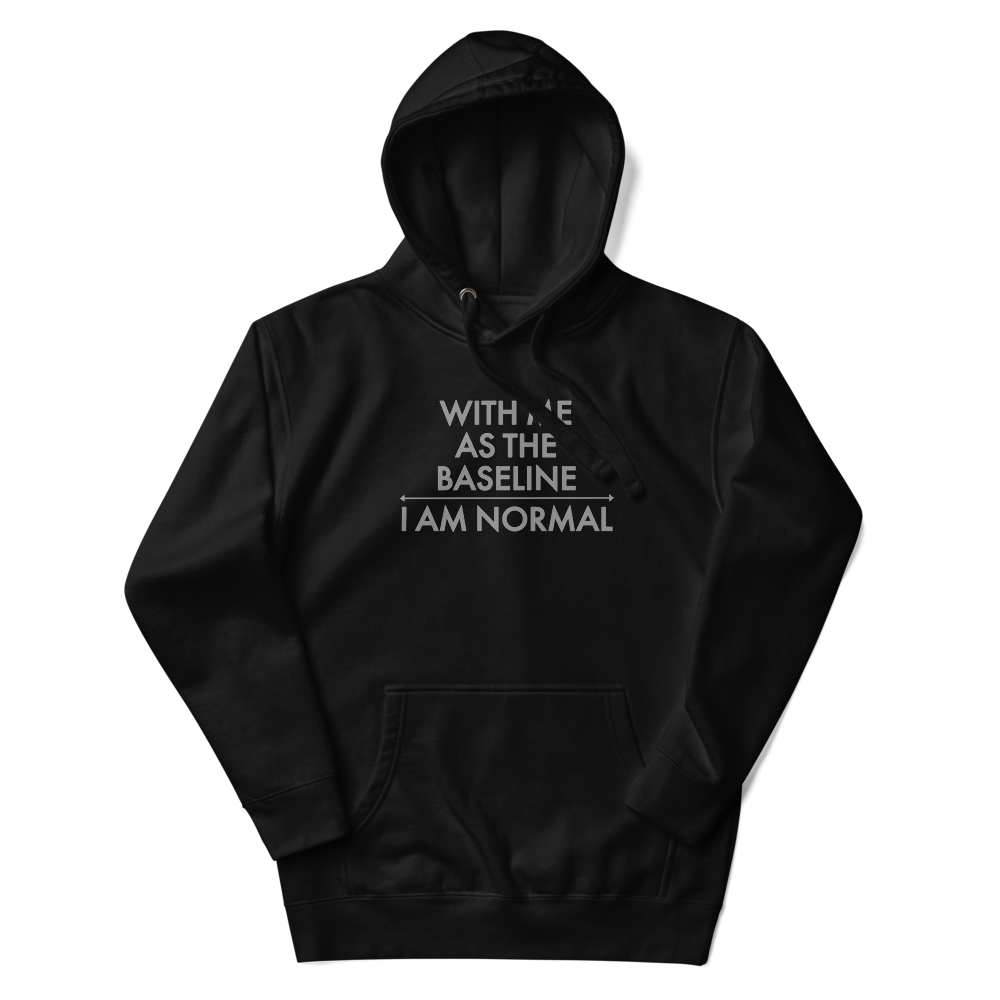 "With me as the baseline, I am normal" printed on a black unisex hoodie laying on a flat surface with the hood up