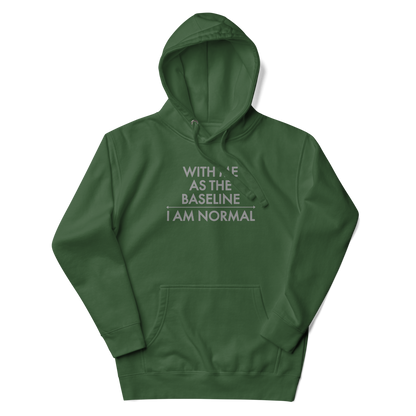 "With me as the baseline, I am normal" printed on a forest green unisex hoodie laying on a flat surface with the hood up