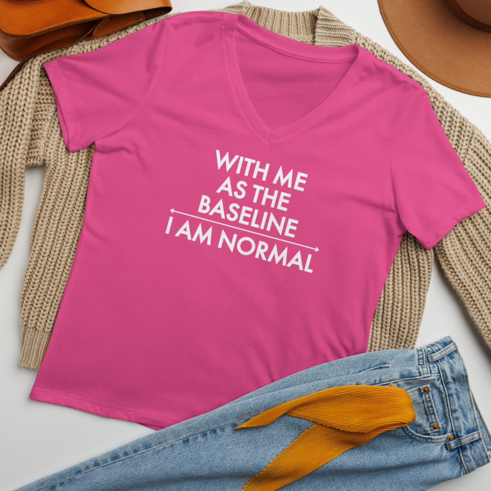 "With me as the baseline, I am normal" printed on a berry women's relaxed v-neck t-shirt laying on a flat surface amongst other clothes