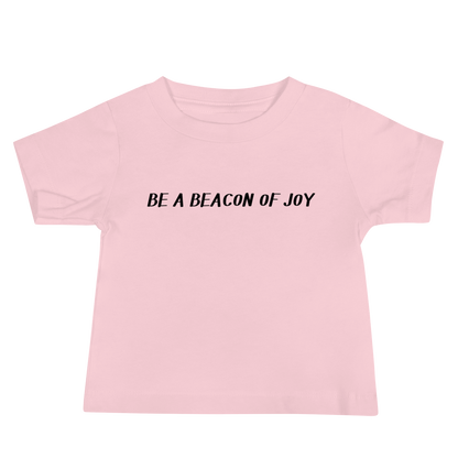 "Be a beacon of joy" printed on a pink baby jersey short sleeve tee laying on a flat surface