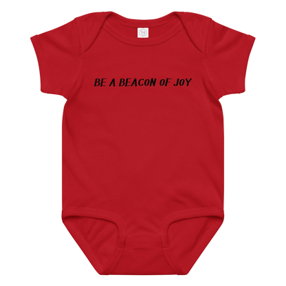 "Be a beacon of joy" printed on a red baby jersey bodysuit laying on a flat surface amongst other clothes