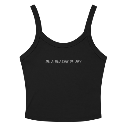 "Be a beacon of joy" printed on a solid black blend women's micro-rib tanktop laying on a flat surface amongst sunglasses and shorts