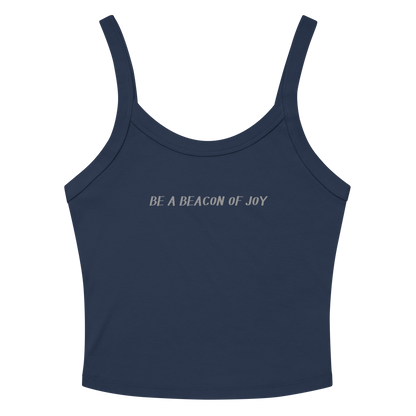 "Be a beacon of joy" printed on a solid navy blend women's micro-rib tanktop laying on a flat surface amongst sunglasses and shorts