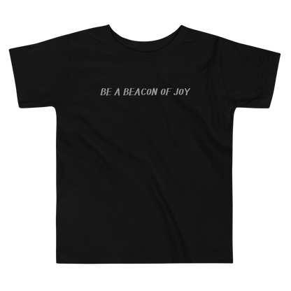"Be a beacon of joy" printed on a black toddler short sleeve tee laying on a flat surface