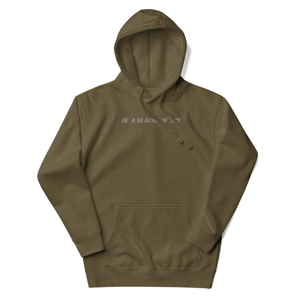 "Be a beacon of joy" printed on a military green unisex hoodie laying on a flat surface with the hood up