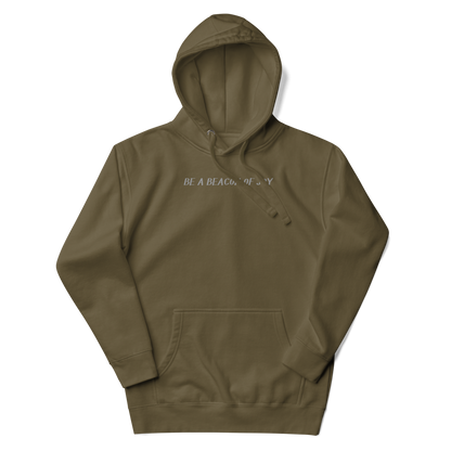 "Be a beacon of joy" printed on a military green unisex hoodie laying on a flat surface with the hood up