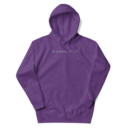 "Be a beacon of joy" printed on a purple unisex hoodie laying on a flat surface with the hood up