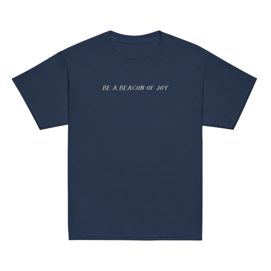 "Be a beacon of joy" printed on a navy youth classic tee laying on a flat surface