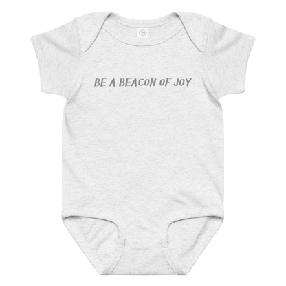 "Be a beacon of joy" printed on a ash baby jersey bodysuit laying on a flat surface amongst other clothes