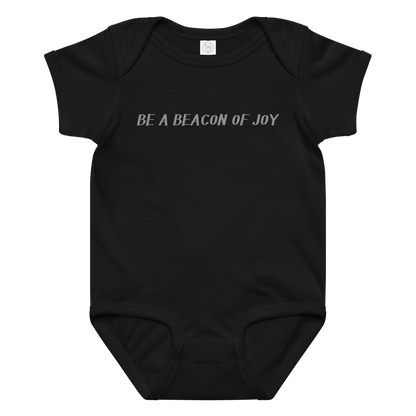 "Be a beacon of joy" printed on a black baby jersey bodysuit laying on a flat surface amongst other clothes