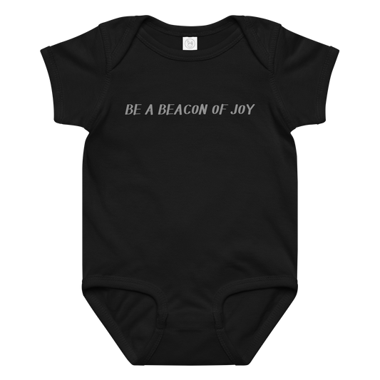 "Be a beacon of joy" printed on a black baby jersey bodysuit laying on a flat surface amongst other clothes