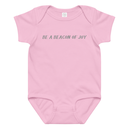 "Be a beacon of joy" printed on a pink baby jersey bodysuit laying on a flat surface amongst other clothes